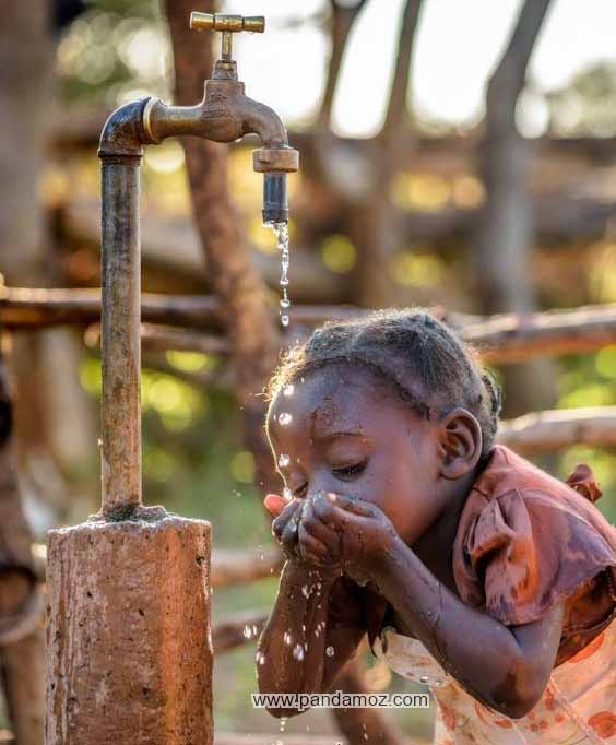 عکس پسربچه رنگین پوست که در حال خوردن آب از شیر آب است و قطرات آب به اطراف می پاشد