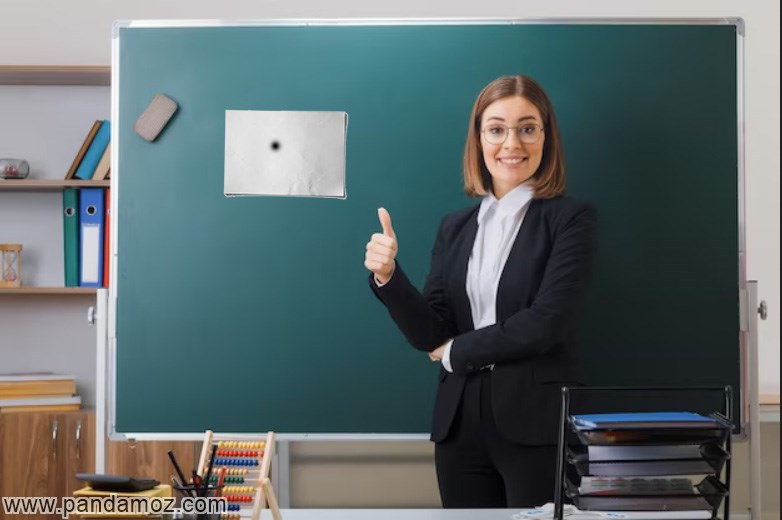 عکس یک خانم معلم در کلاس که کاغذ سفیدی را بر روی تخته سیاه چسبانده و روی وسط آن کاغذ نقطه سیاه وجود دارد. در تصویر کلاس درس است و معلم لباس فرم سرمه ایی پوشیده و با انگشت به کاغذ روی تخته سیاه اشاره می کند