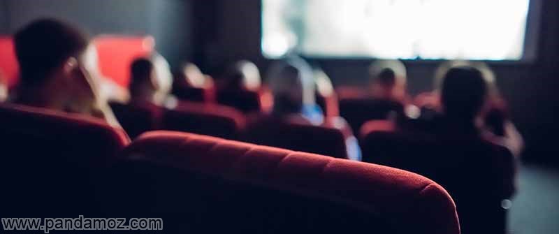 عکس مردم در سینما. تصویر به صورت مات بوده و از پشت سر مردمی را نشان می دهد که روی مبل های مخمل قرمز رنگ سینما نشسته و پرده فیلم را تماشا می کنند